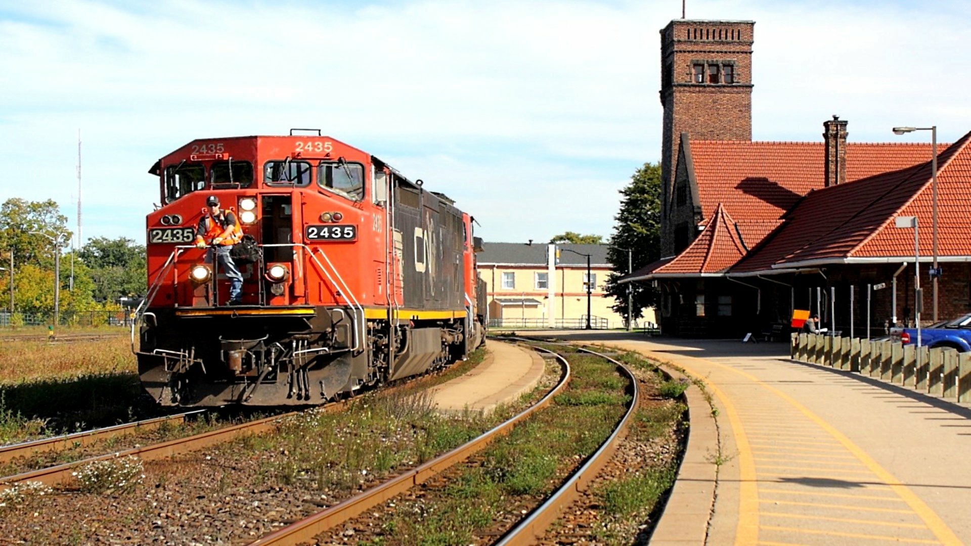 HD desktop wallpaper showcasing a vibrant red train approaching a classic station building under a clear sky.