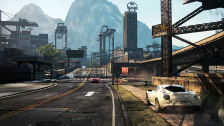 A dynamic HD wallpaper from Need For Speed: Most Wanted, featuring a sleek white sports car parked beside an urban road, surrounded by mountains and industrial structures.