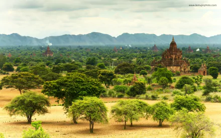 A serene landscape featuring lush greenery and ancient temples, set against a backdrop of rolling mountains. This HD wallpaper beautifully captures a peaceful religious atmosphere.