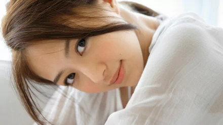 HD desktop wallpaper featuring an Asian woman with soft features, gently smiling and gazing directly at the camera, creating a calm and inviting background.