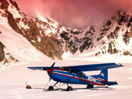 HD PC desktop wallpaper/background — blue Cessna light aircraft parked on a snowy airstrip beneath pink‑tinted alpine peaks.
