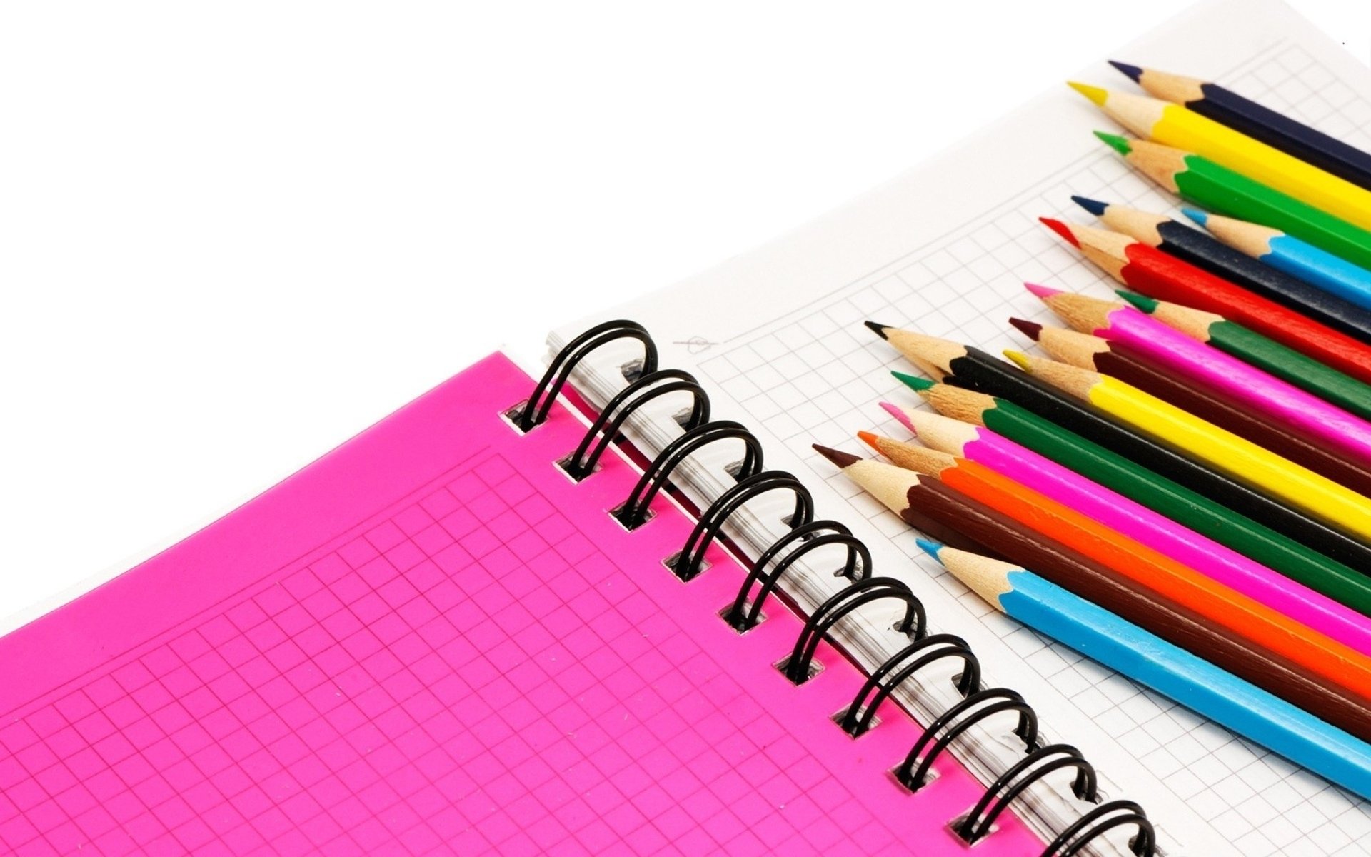 HD desktop wallpaper photography: close-up of a spiral pink notebook beside a fanned set of sharpened colored pencils on a clean white background.