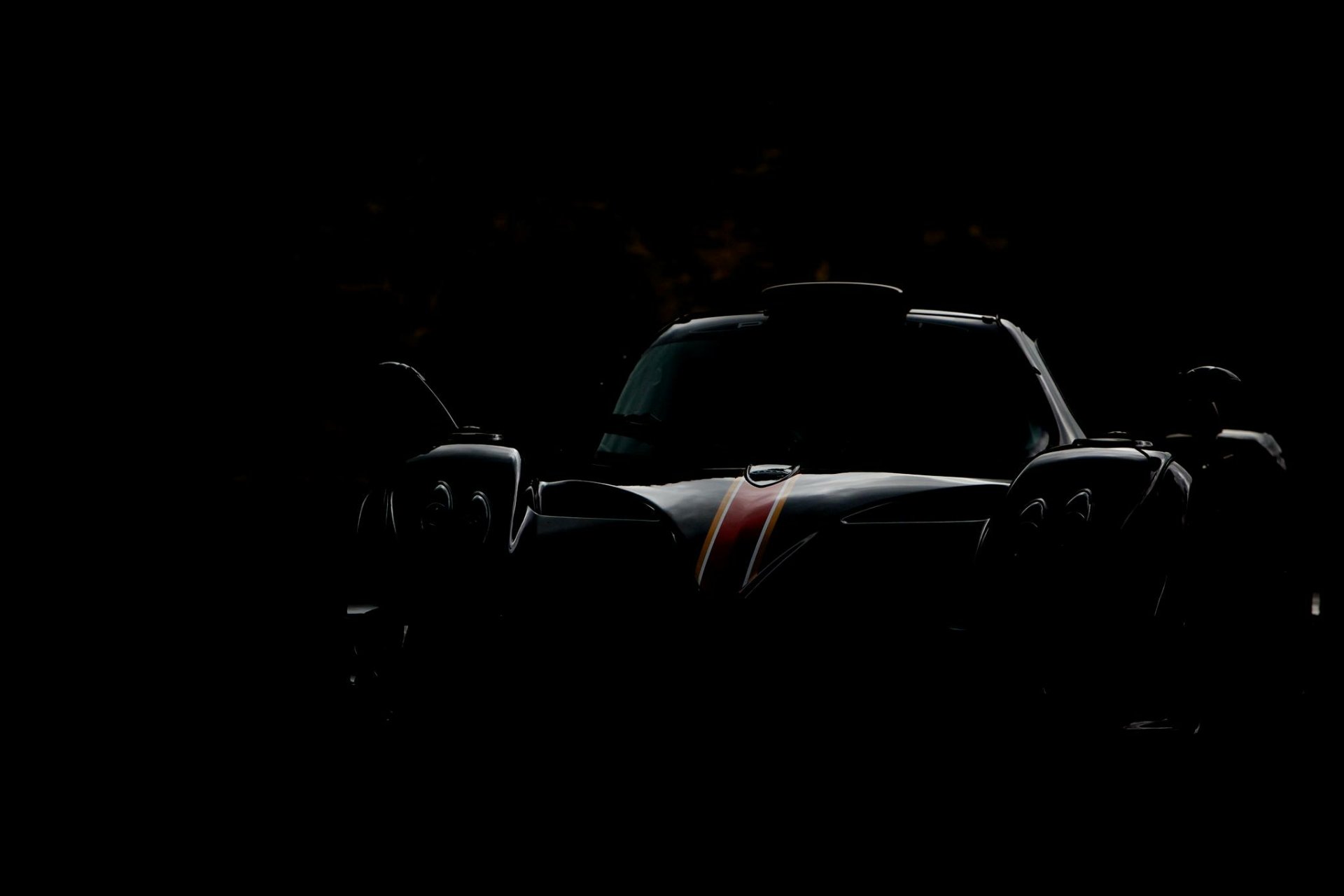 HD PC desktop wallpaper of a Pagani vehicle: a hypercar silhouette with a red hood stripe emerging from a deep black background.