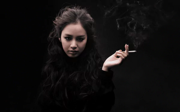 A captivating HD wallpaper featuring a woman with long dark hair and a cigarette, set against a dramatic black background, reflecting a mysterious and intriguing aura.