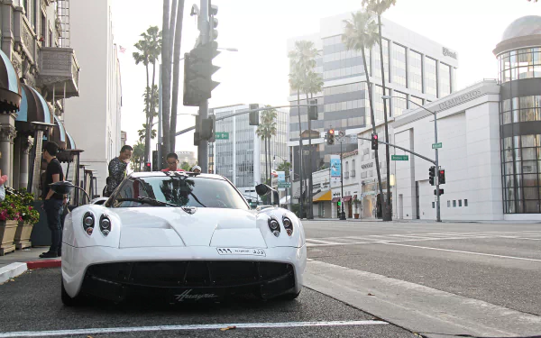 HD PC desktop wallpaper featuring a white Pagani Huayra parked on a city street with palm trees and modern buildings in the background.