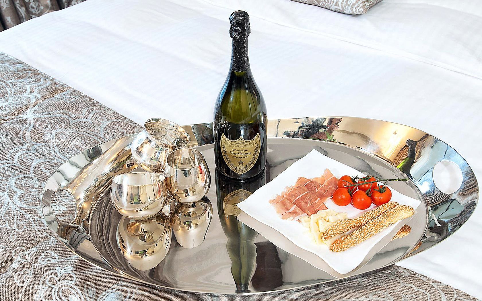 HD PC desktop wallpaper and background — breakfast food tray on a bed with a bottle of sparkling wine, stemless glasses, prosciutto, cherry tomatoes and breadsticks on a silver platter.