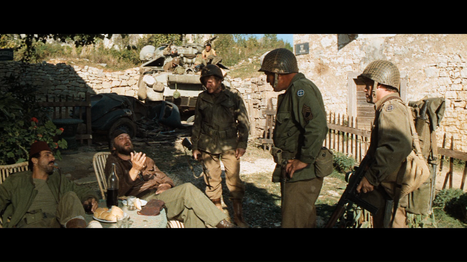 HD PC desktop wallpaper of the movie Kelly's Heroes: World War II soldiers in helmets and uniforms gathered and talking in a sunlit village courtyard.