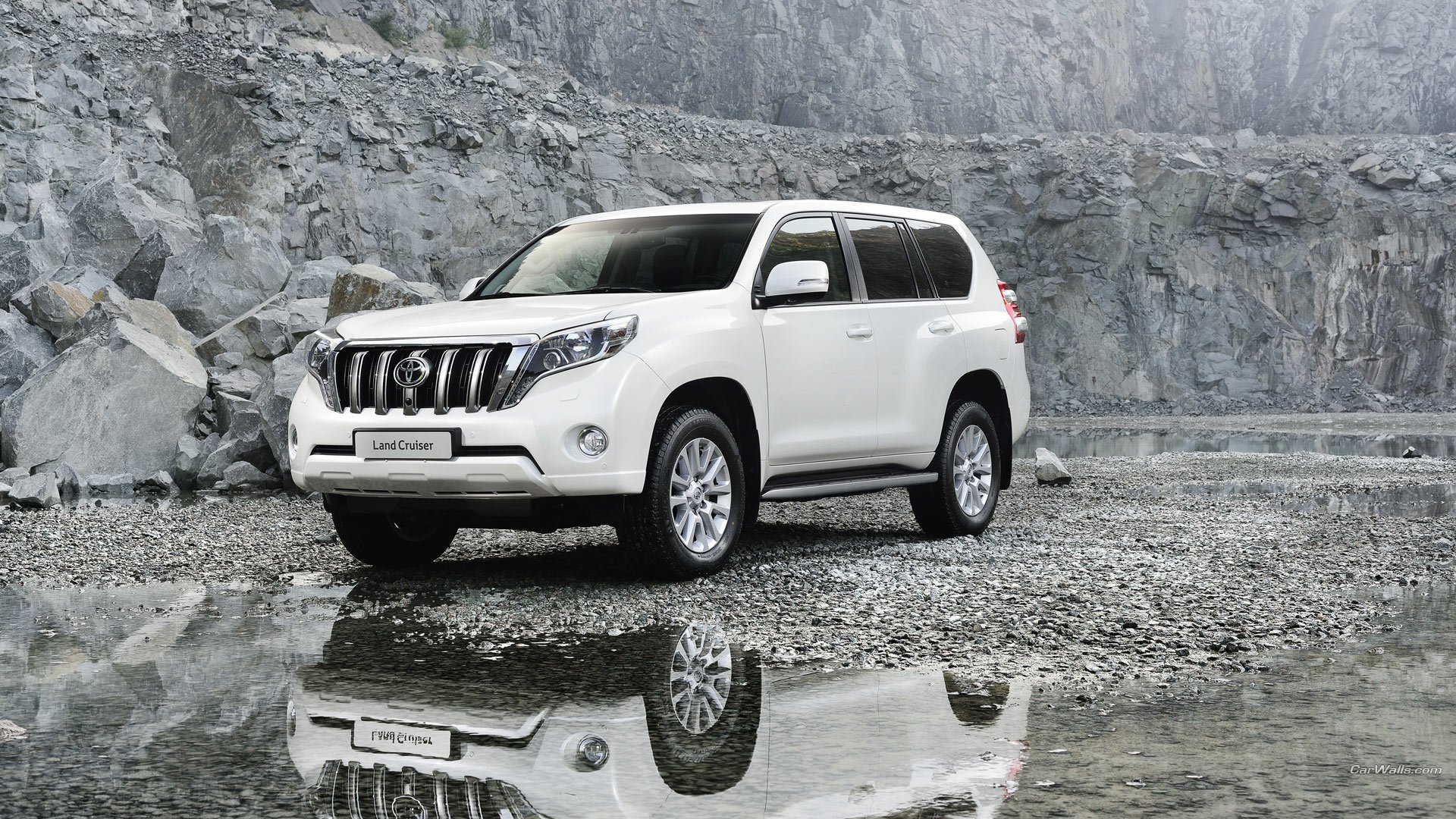 A white 2014 Toyota Land Cruiser parked on rocky terrain with a clear reflection in water, featured as an HD PC desktop wallpaper and background.
