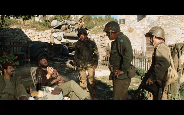HD PC desktop wallpaper of the movie Kelly's Heroes: World War II soldiers in helmets and uniforms gathered and talking in a sunlit village courtyard.