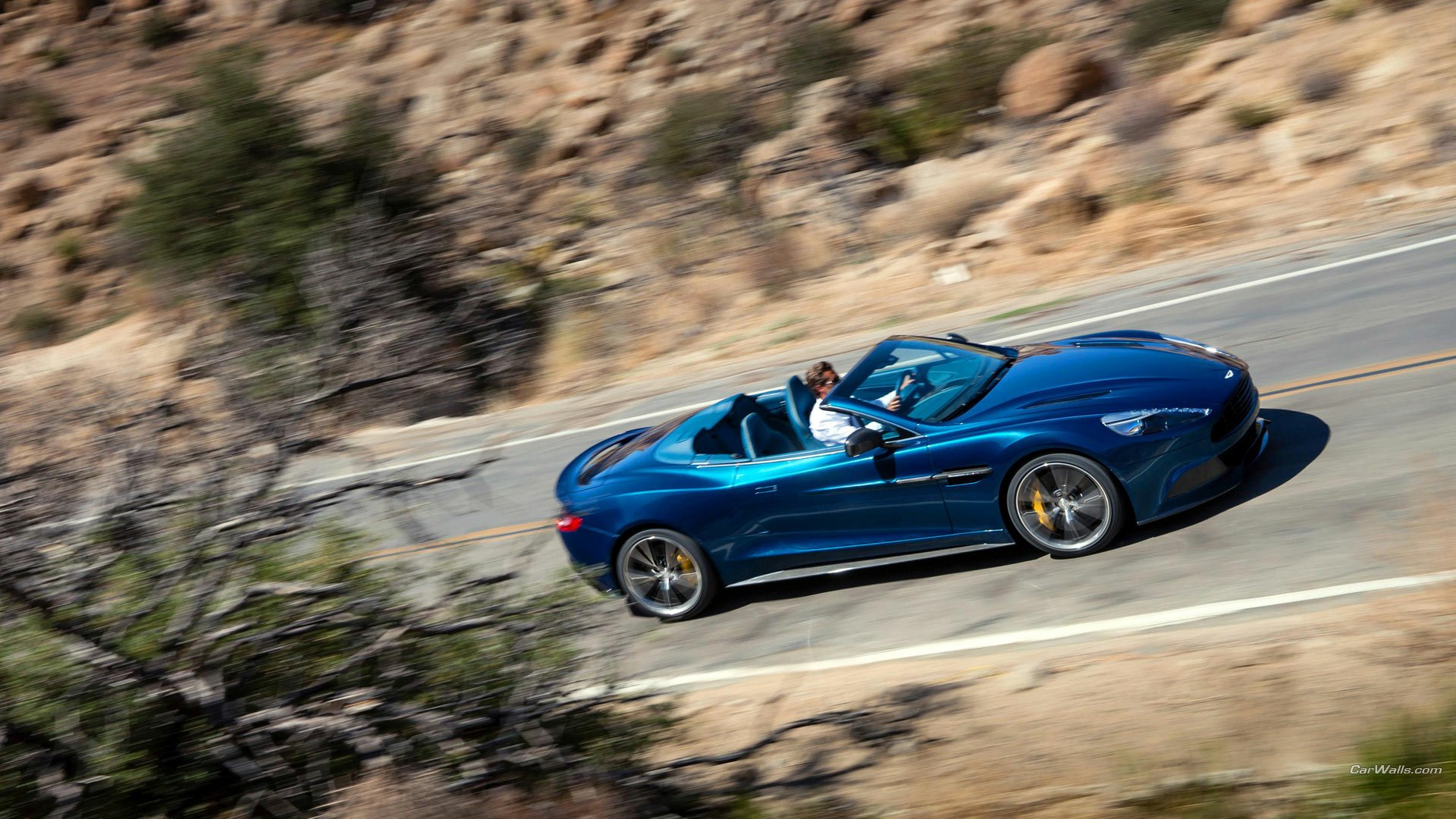 Blue 2014 Aston Martin Vanquish Volante convertible on a winding desert road, captured as an HD PC desktop wallpaper/background.