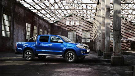HD PC desktop wallpaper featuring a blue Toyota Hilux parked inside an old industrial building with dramatic light and shadows.