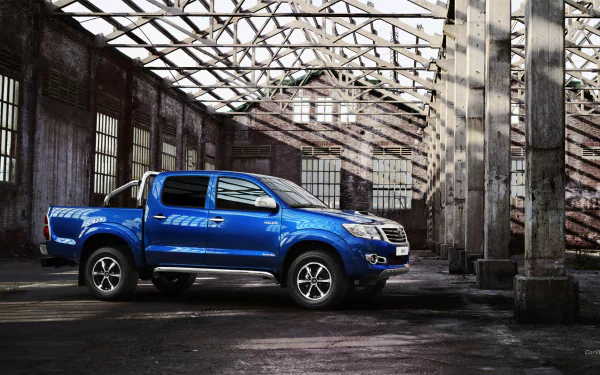 HD PC desktop wallpaper featuring a blue Toyota Hilux parked inside an old industrial building with dramatic light and shadows.