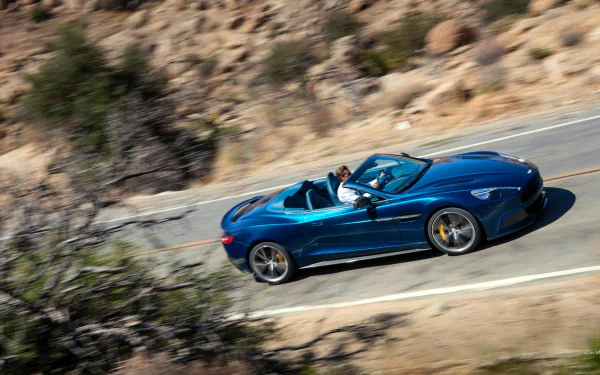 Blue 2014 Aston Martin Vanquish Volante convertible on a winding desert road, captured as an HD PC desktop wallpaper/background.