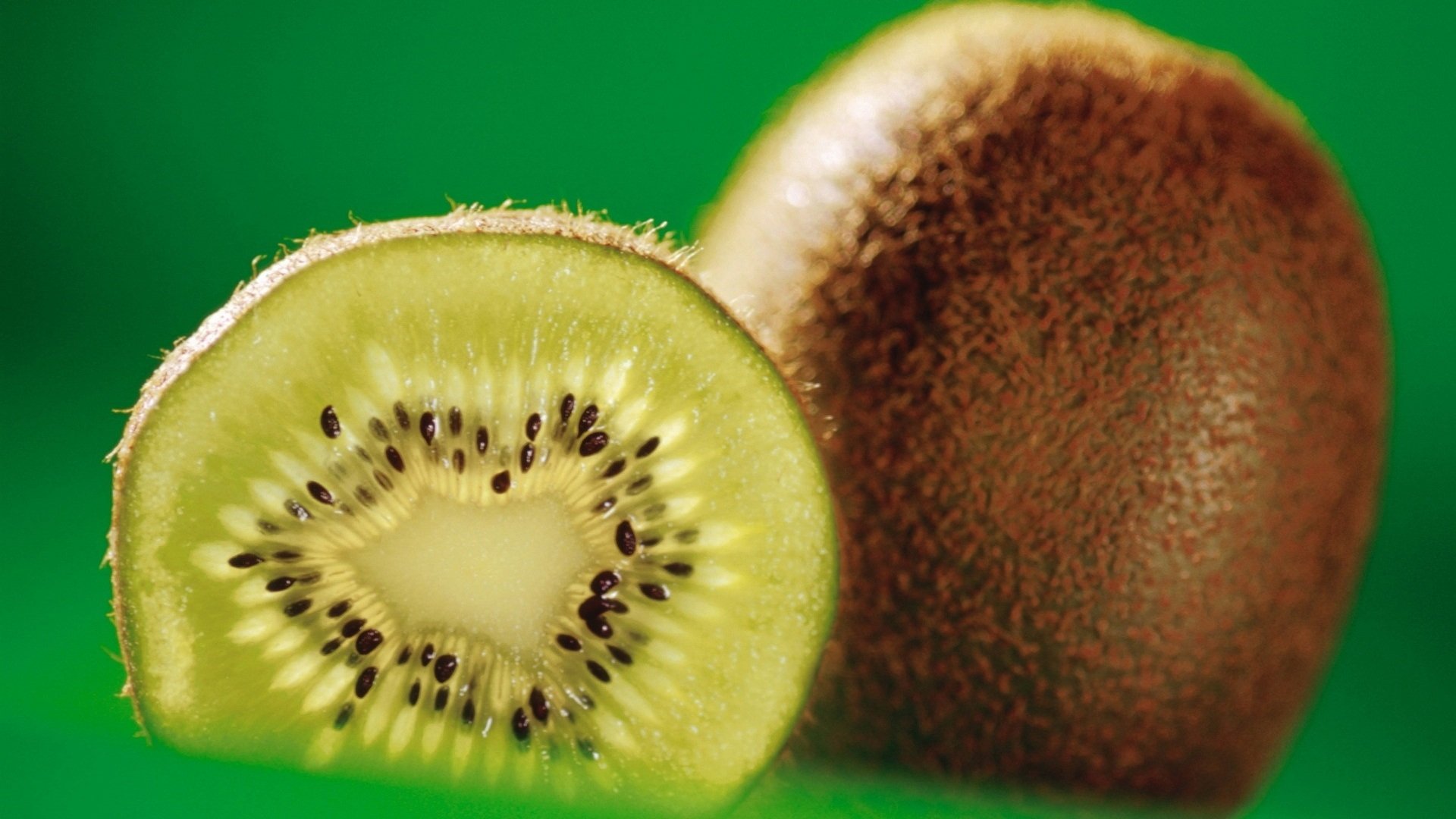HD PC desktop wallpaper/background of fresh kiwi: a whole fuzzy brown fruit beside a bright green sliced half with seeds on a vivid green background.