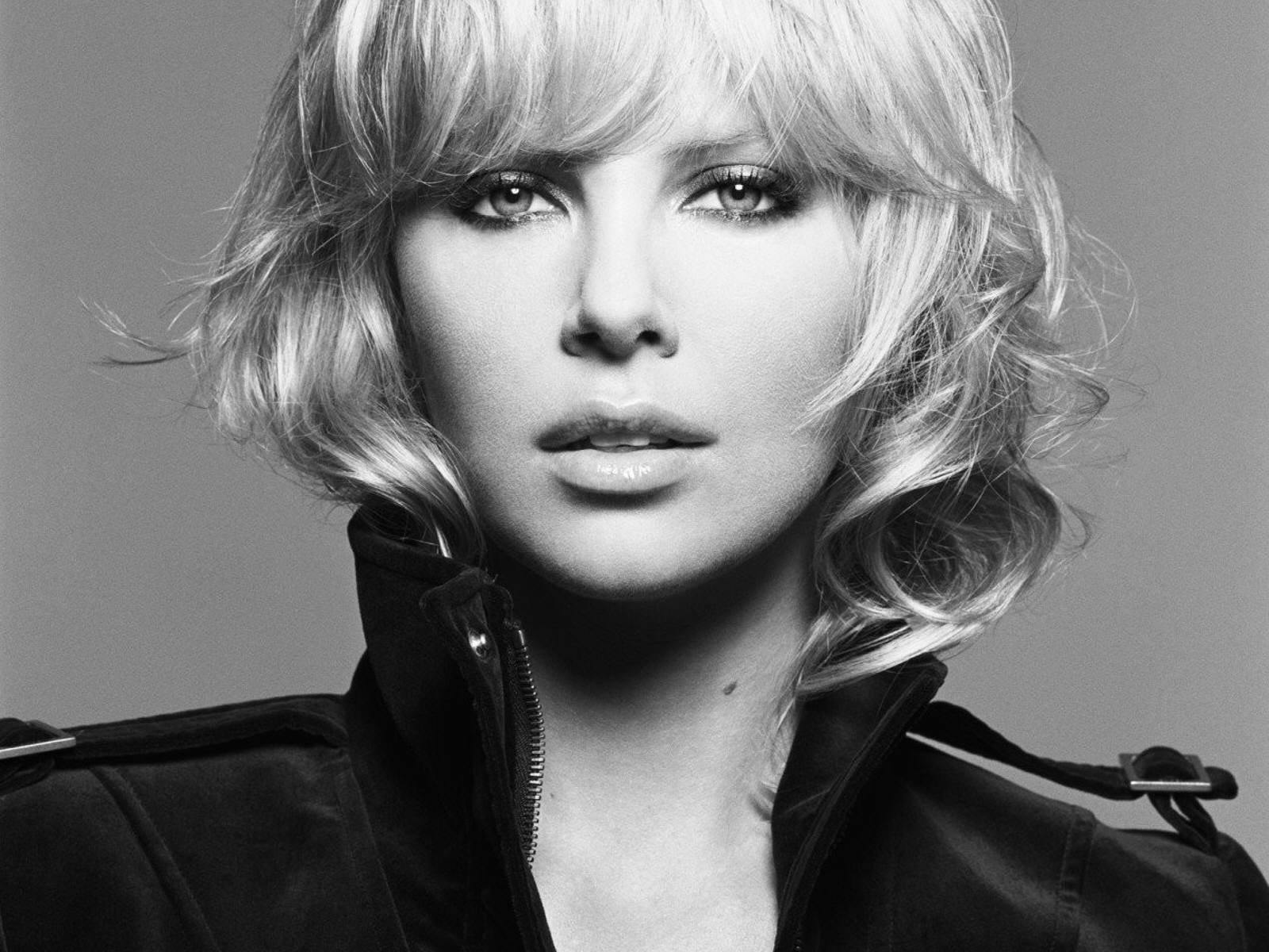 Black and white HD desktop wallpaper featuring a close-up portrait of celebrity Charlize Theron with tousled hair and intense gaze.