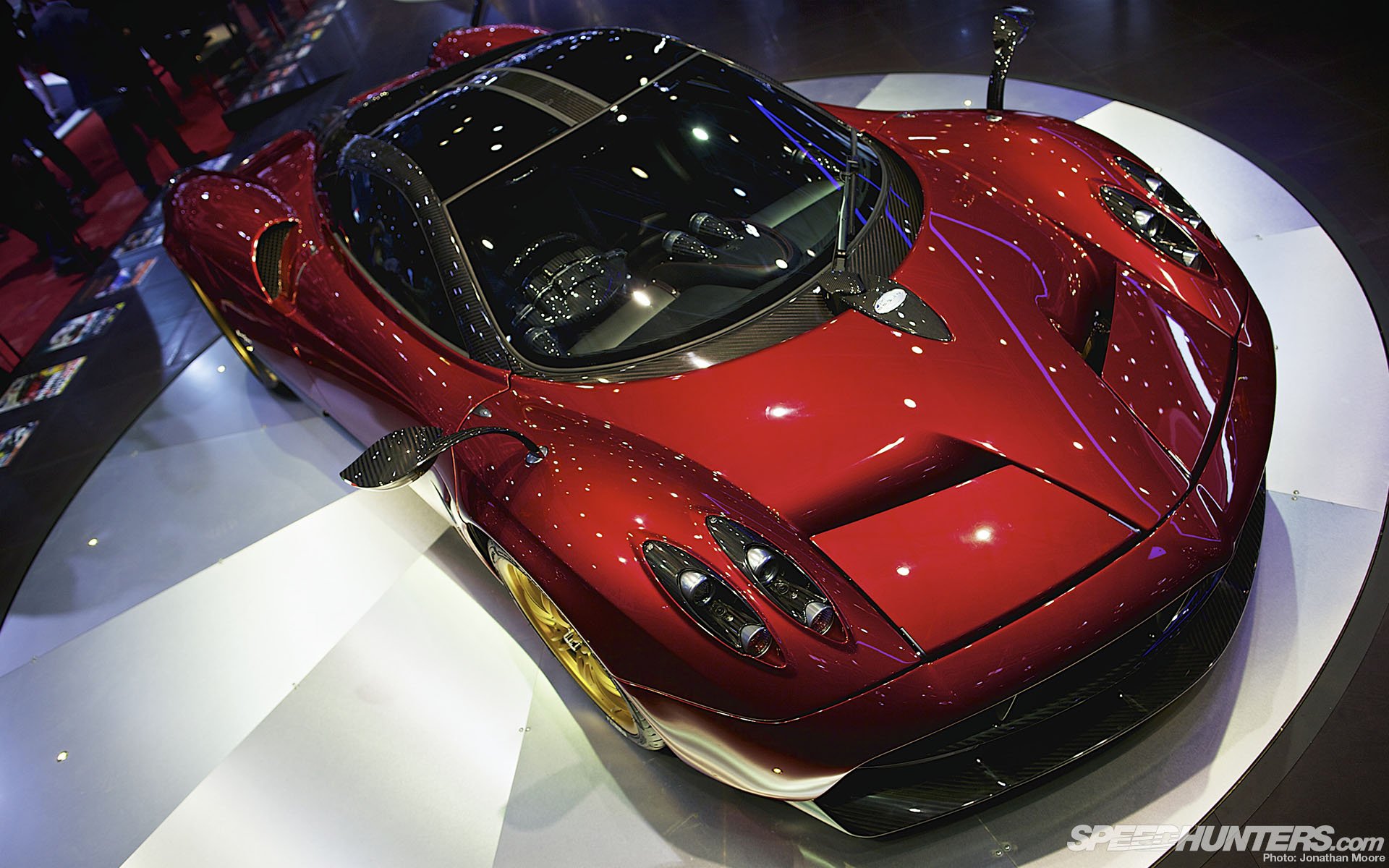 HD desktop wallpaper featuring a sleek red Pagani Huayra sports car displayed in a showroom setting.