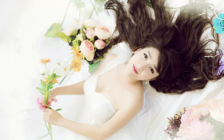HD desktop wallpaper and background featuring a beautiful bride lying down with flowing hair, holding flowers. She wears a white wedding dress, surrounded by various flower arrangements.