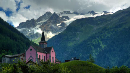 HD desktop wallpaper of a pink religious chapel nestled in a lush green forest with towering mountains in the background under a cloudy sky.