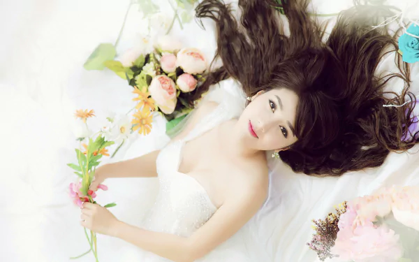 HD desktop wallpaper and background featuring a beautiful bride lying down with flowing hair, holding flowers. She wears a white wedding dress, surrounded by various flower arrangements.