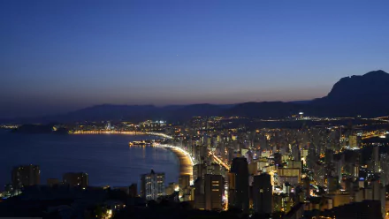 A breathtaking evening view of Benidorm's beach and coastline, illuminated by city lights, showcasing the harmony of man-made structures with the natural beauty of the coast.