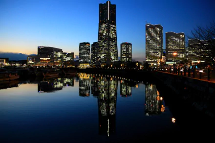 HD desktop wallpaper of Yokohama’s illuminated skyline at dusk, featuring modern man-made skyscrapers reflecting on calm water.