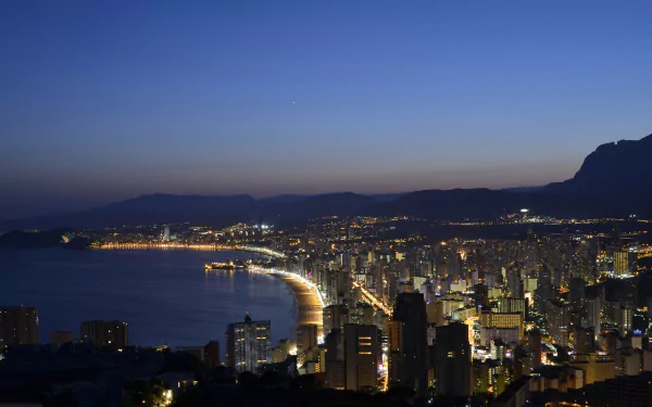 A breathtaking evening view of Benidorm's beach and coastline, illuminated by city lights, showcasing the harmony of man-made structures with the natural beauty of the coast.