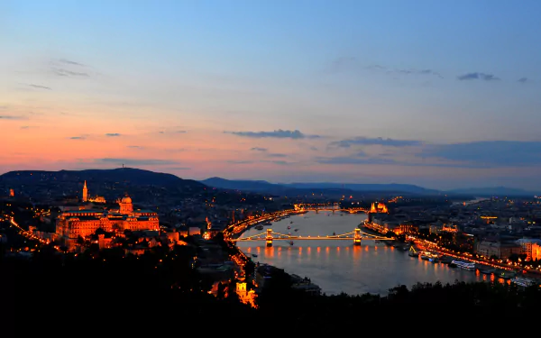 Nighttime panoramic view of Budapest, Hungary, showcasing illuminated landmarks and bridges along the Danube River under a colorful evening sky.