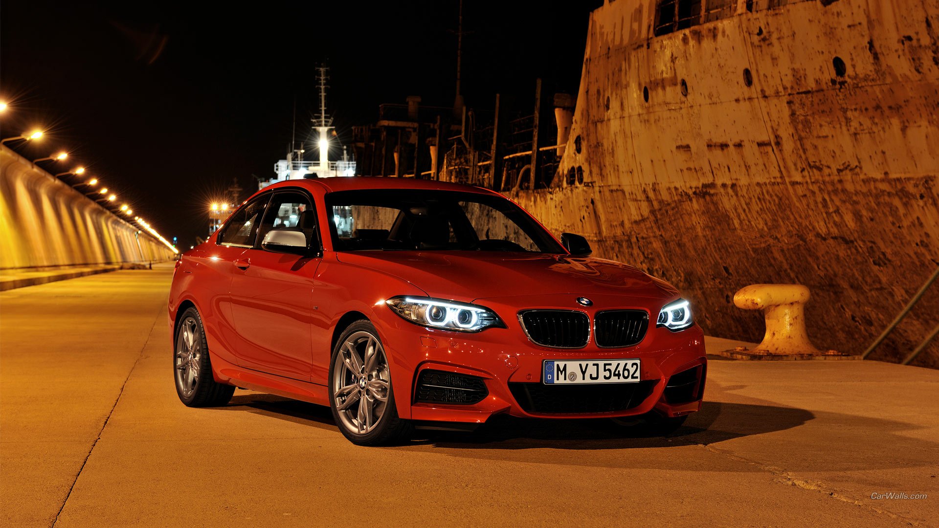 Red BMW M235i Coupe parked on a dimly lit dock at night with illuminated headlights and glossy finish — HD PC desktop wallpaper/background.