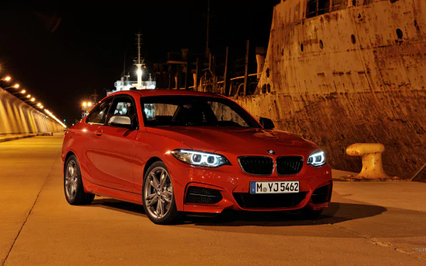 Red BMW M235i Coupe parked on a dimly lit dock at night with illuminated headlights and glossy finish — HD PC desktop wallpaper/background.