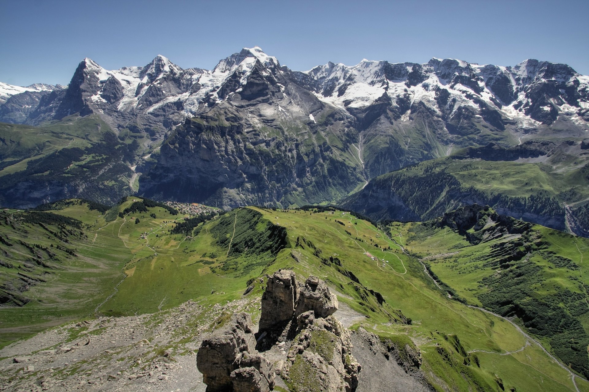 2K Quad HD PC desktop wallpaper/background — nature mountain panorama: snow-capped peaks rising above green alpine valleys with rocky foreground.