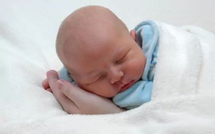 HD photography of a peacefully sleeping baby wrapped in a soft white blanket, featured as a serene PC desktop wallpaper background.