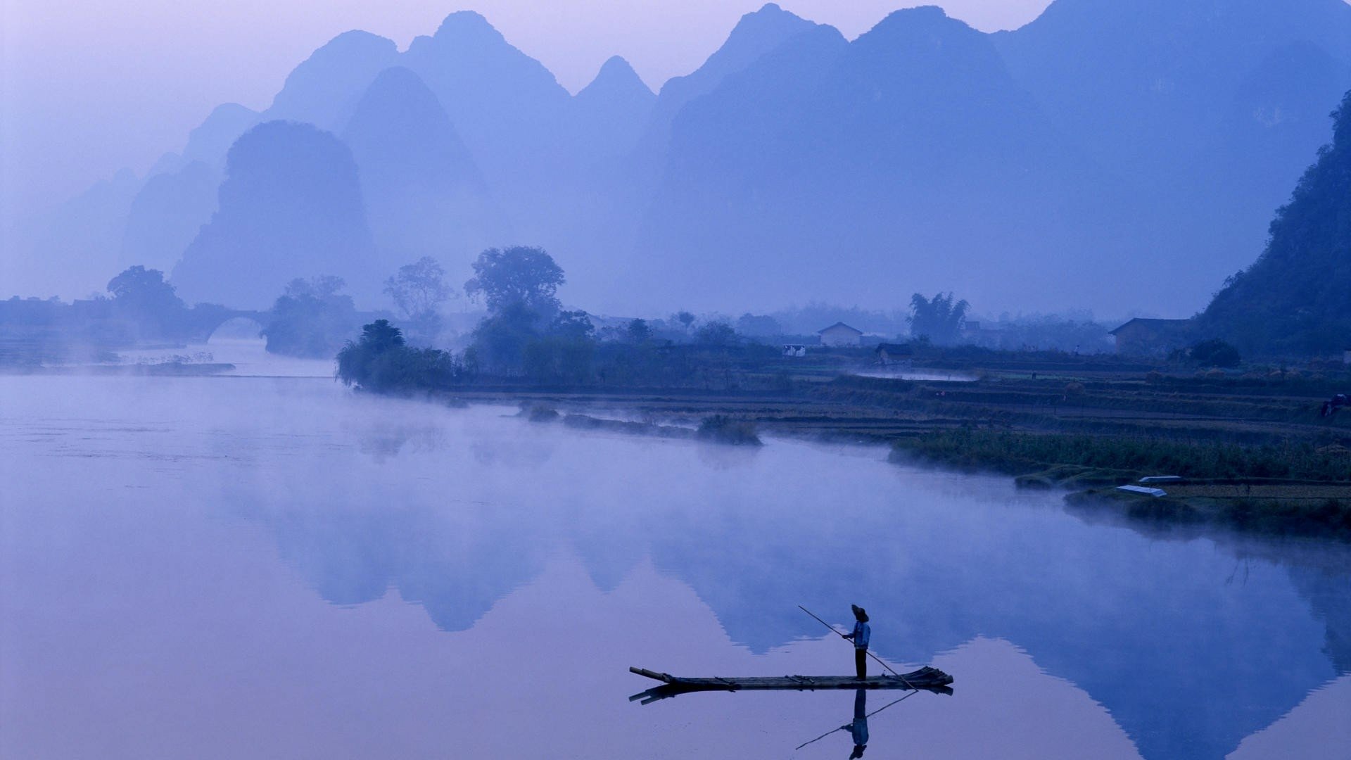 HD photography wallpaper showing a serene river scene with misty mountains and a lone fisherman reflected in calm water, capturing peaceful natural beauty and reflection.