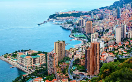 HD desktop wallpaper showcasing a vibrant man-made cityscape of Monaco along the coastline with densely packed buildings and blue Mediterranean waters.