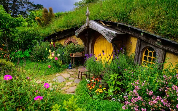 A vibrant, man-made Hobbiton scene featuring a charming round yellow door house surrounded by lush greenery and colorful flowers, captured in HD for a PC desktop wallpaper.