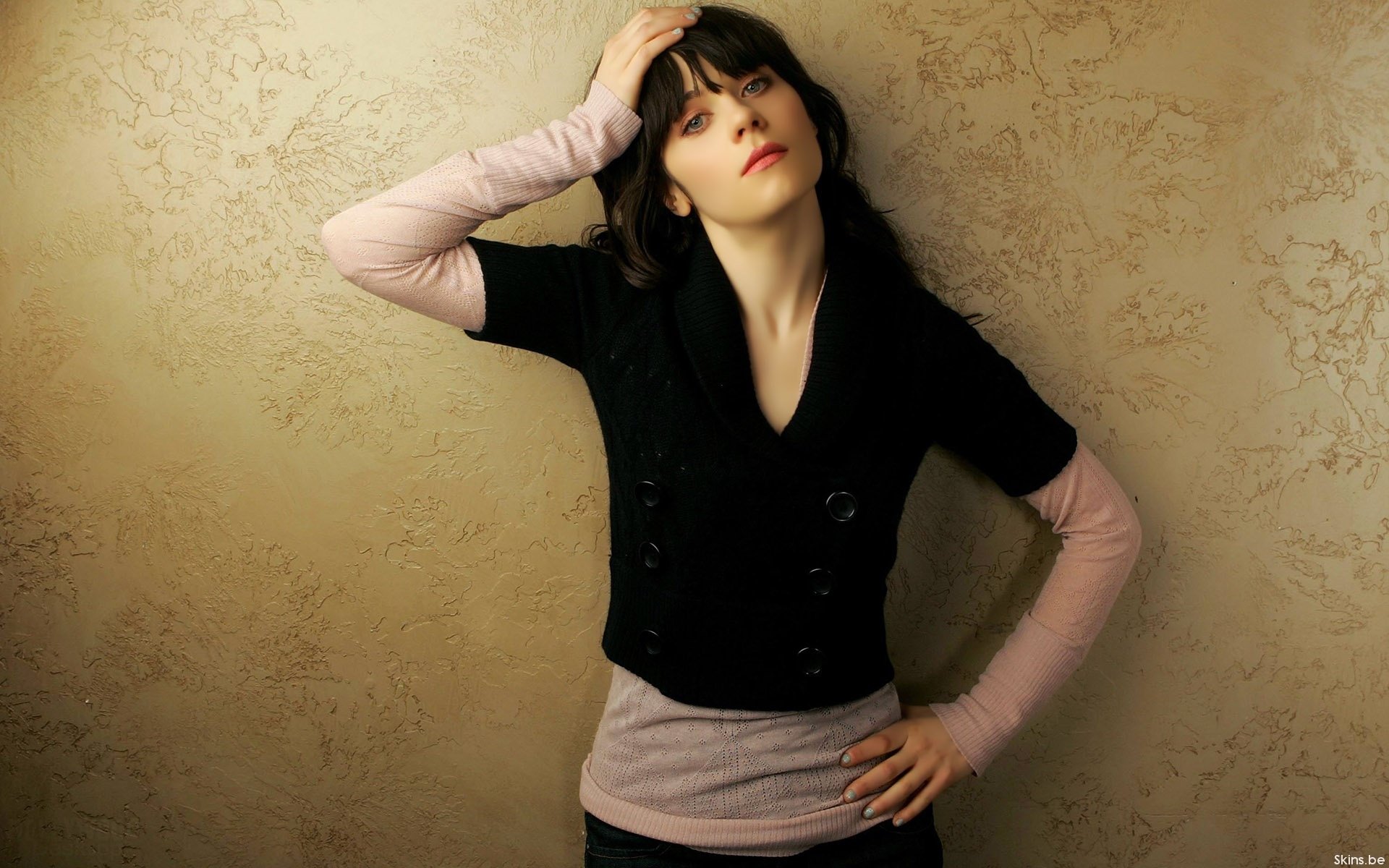 HD desktop wallpaper featuring celebrity Zooey Deschanel striking a casual pose against a textured beige background.