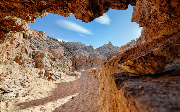 4K Ultra HD PC desktop wallpaper: sunlit rocky canyon passage seen through a cave opening, sandy floor and bright blue sky.