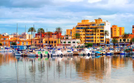HD desktop wallpaper of a vibrant Palma de Mallorca harbor with boats docked and colorful man-made buildings reflecting on calm water.