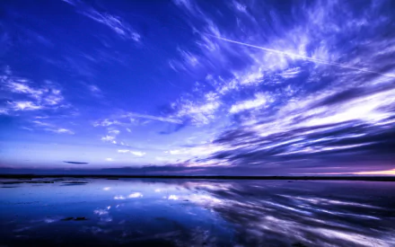 A serene nature scene featuring a vibrant sky, with dramatic clouds reflecting in calm waters. This HD wallpaper adds a tranquil touch to any desktop background.