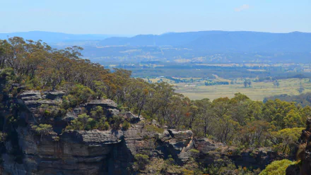 HD PC desktop wallpaper of Australia’s Blue Mountains: tree-dotted rocky cliffs, sweeping valley and distant mountain ridges under a clear blue sky