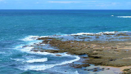 A vibrant HD desktop wallpaper showcasing the Norah Head coastline in Australia with ocean waves crashing against rocky shores under a clear horizon.