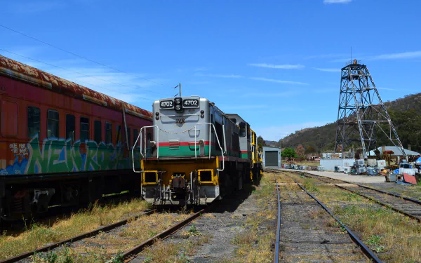 HD PC desktop wallpaper showing a Lithgow locomotive train and rail vehicles on sunlit sidings beside an old tower under a bright blue sky.