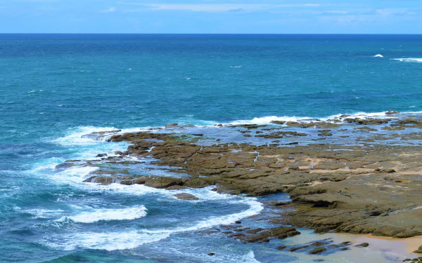 A vibrant HD desktop wallpaper showcasing the Norah Head coastline in Australia with ocean waves crashing against rocky shores under a clear horizon.