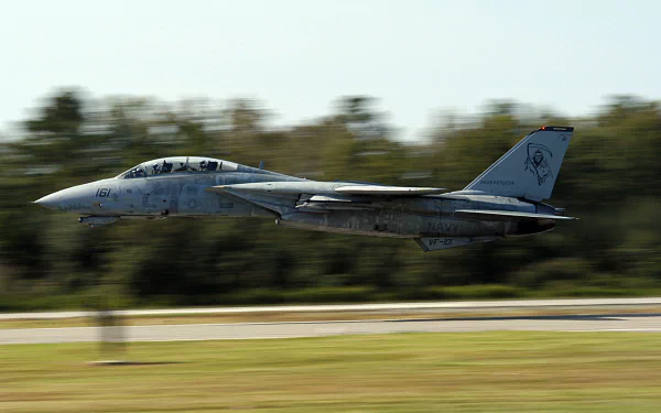 HD desktop wallpaper showcasing a military Grumman F-14 Tomcat jet in flight, captured with motion blur against a blurred forest background.