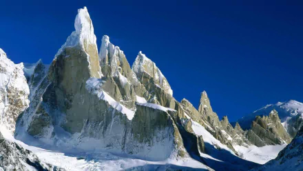 Snow-covered jagged cliffs rise sharply under a clear blue sky at sunrise in Los Glaciares National Park, Argentina, showcasing a stunning snowy mountain peak.