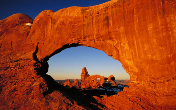 HD PC desktop wallpaper featuring a natural rock arch formation with a vibrant orange hue against a clear blue sky in a scenic nature setting.