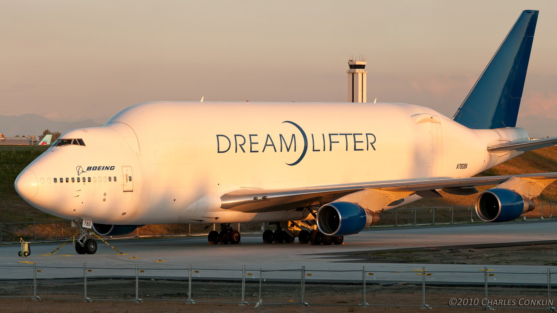 HD desktop wallpaper: Boeing 747 Dreamlifter cargo airplane on the taxiway at sunset, vehicle profile with prominent DREAMLIFTER logo.