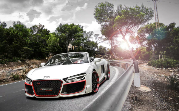 HD desktop wallpaper image of an Audi R8 Spyder on a scenic road, surrounded by lush greenery and bathed in sunlight. The white Audi R8 stands out with its sporty design and luxurious appeal.