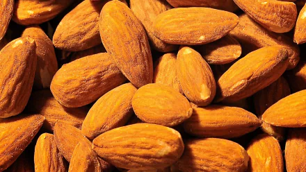 Close-up of a pile of almonds, showcasing their rich brown tones and textured surfaces, creating a vibrant and appealing HD desktop wallpaper background.