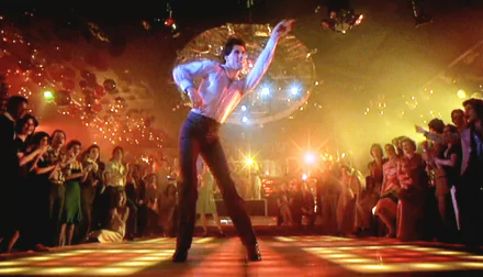 HD desktop wallpaper of a disco dancer in a white suit striking a dramatic pose beneath a mirrored ball — iconic Saturday Night Fever scene featuring Tony Manero.
