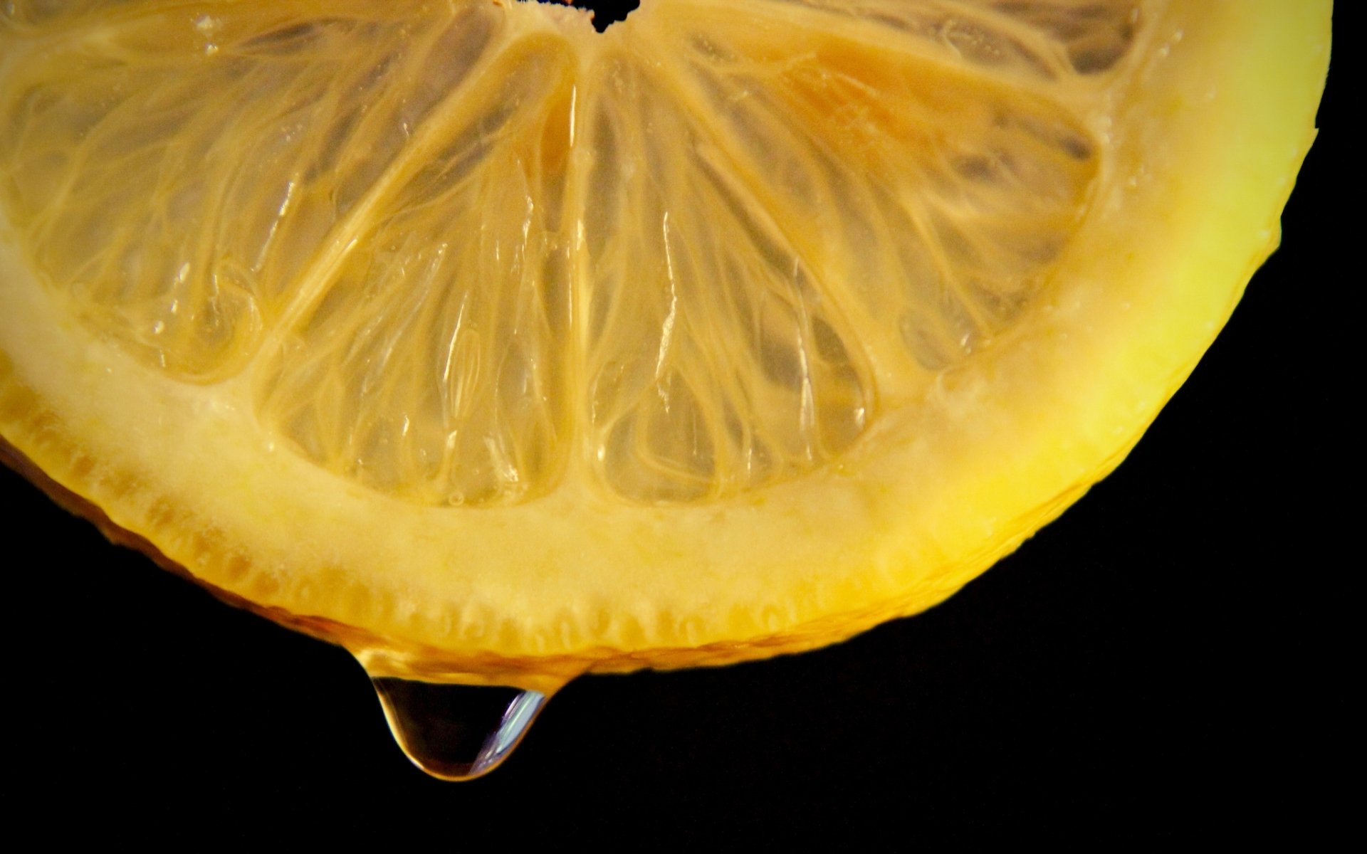 Close-up HD desktop wallpaper of a lemon slice with a drop of juice hanging, highlighting its vibrant texture against a black background.
